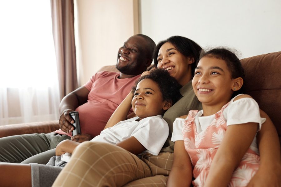 Family of four sitting together on cough watching TV.