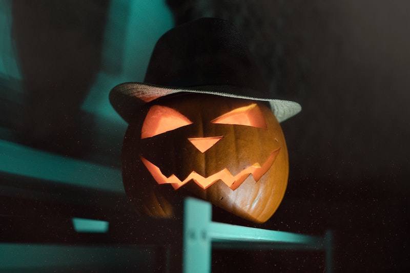 Carved pumpkin on ledge wearing hat.