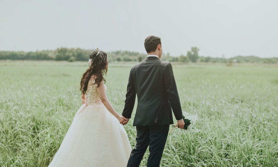 Young bride and groom walking through green field.