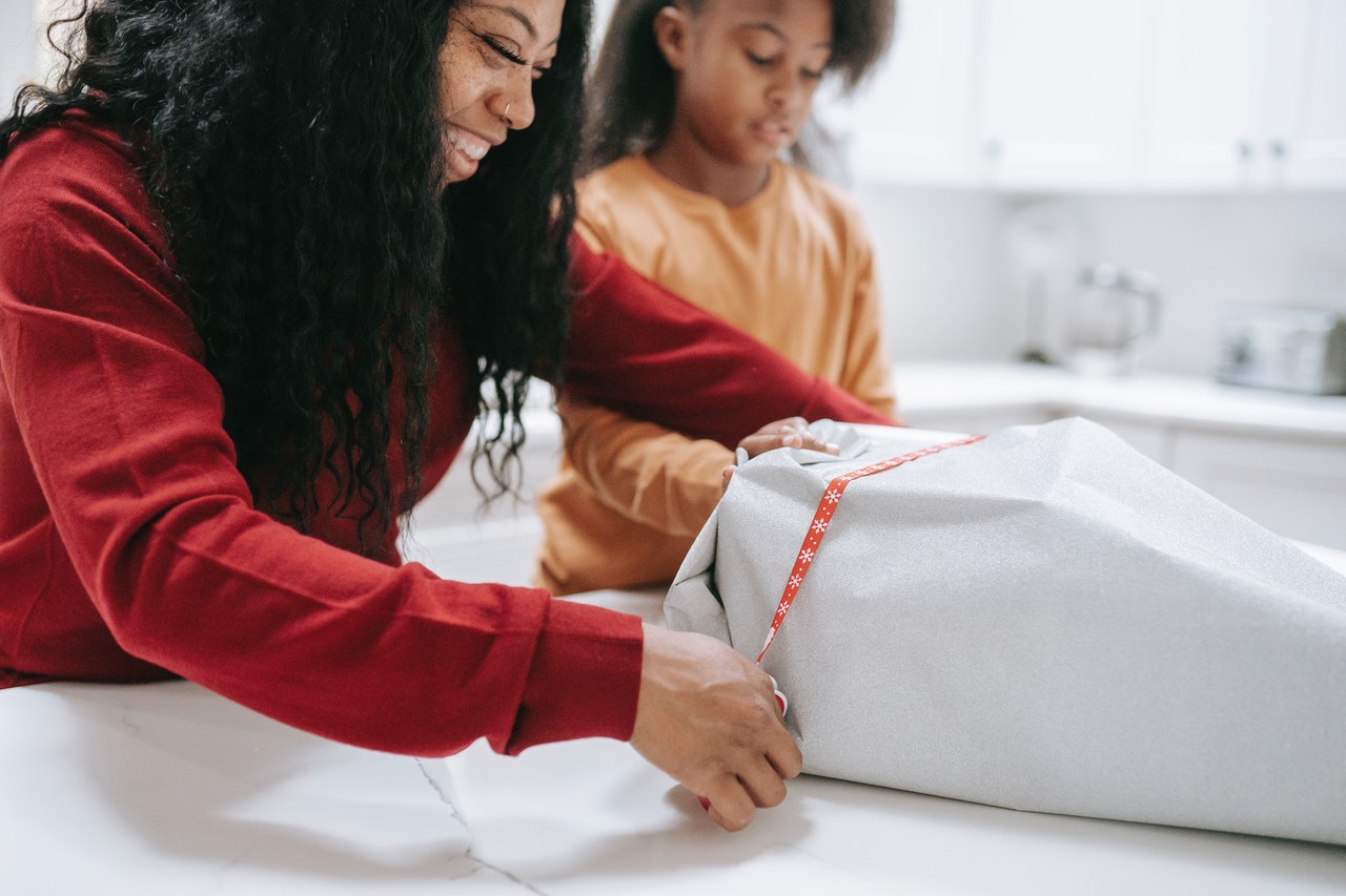 Young mother wrapping Christmas gift with daughter.