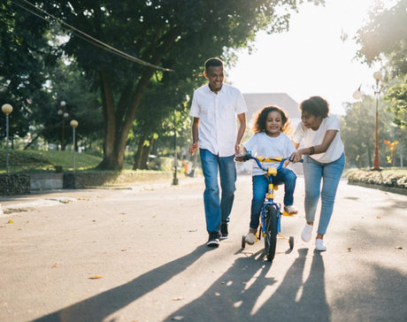 Young parents helping daughter ride her bike.