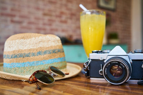 camera on table next to vacation hat and sunglasses